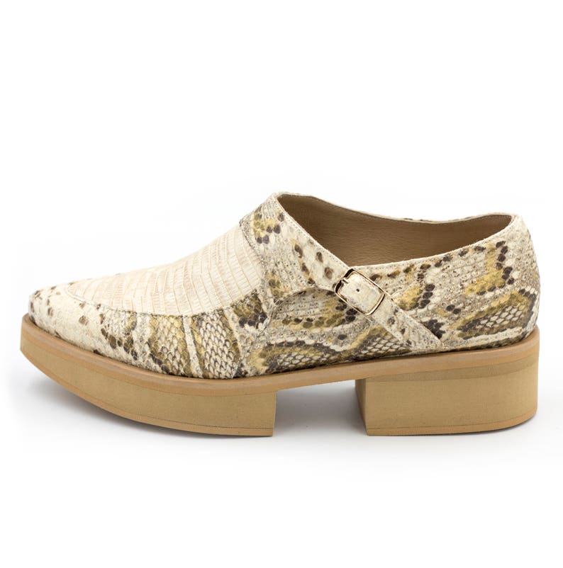 Puede incluir: Un par de zapatos de plataforma beige con estampado de piel de serpiente y una hebilla.