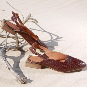 Op de afbeelding: Een paar bruine leren slingback schoenen met een krokodillenprint. De schoenen hebben een vierkante neus en een gespsluiting.