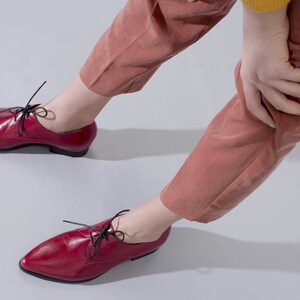 May include: A pair of red leather lace-up shoes with black laces. The shoes have a pointed toe and a low heel.
