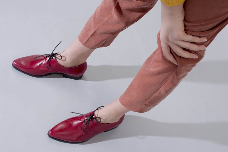 May include: A pair of red leather lace-up shoes with black laces. The shoes have a pointed toe and a low heel.