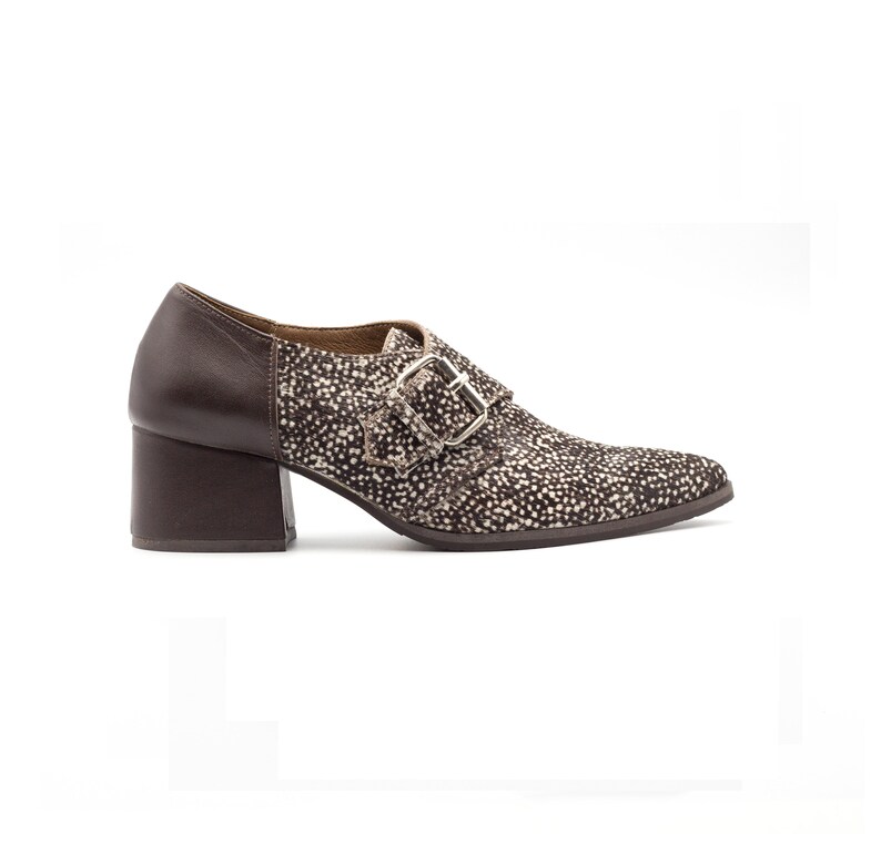 May include: Brown leather heeled shoes with a buckle closure and a spotted pattern on the upper part of the shoe.