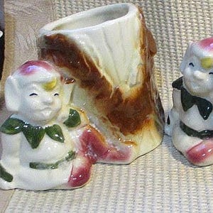 Könnte beinhalten: Vintage Keramik-Pflanzgefäße mit Elfenfiguren. Die Pflanzgefäße haben ein weißes und braunes Baumstammdesign mit roten, grünen und gelben Akzenten. Die Elfenfiguren lächeln und verleihen den Pflanzgefäßen eine verspielte Note.