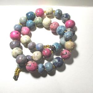 May include: A necklace featuring a strand of colorful, speckled beads in shades of pink, blue, cream, and gray. The beads are strung together with a gold-colored chain and clasp. The necklace is displayed against a white background.