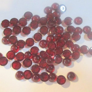 May include: A pile of small, round, red glass cabochons. The cabochons are smooth and shiny.