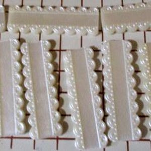 May include: Eight white satin ribbon embellishments with scalloped edges. Each ribbon is approximately 2 inches wide and 4 inches long.