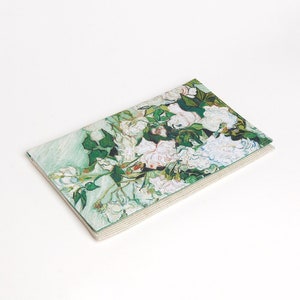 May include: A white and green rectangular fabric clutch with a floral print of white roses and green leaves. The clutch has a white border.