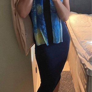 Puede incluir: Una mujer con un vestido azul marino, una bufanda con estampado azul y amarillo, una diadema rosa y tacones beige. Est&aacute; sosteniendo un tel&eacute;fono m&oacute;vil azul claro en su mano derecha.