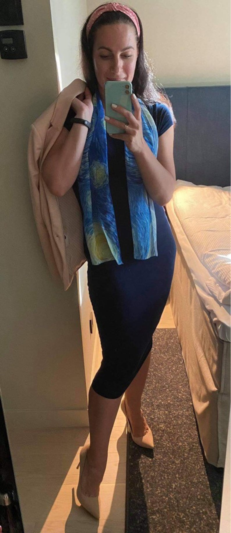 Puede incluir: Una mujer con un vestido azul marino, una bufanda con estampado azul y amarillo, una diadema rosa y tacones beige. Est&aacute; sosteniendo un tel&eacute;fono m&oacute;vil azul claro en su mano derecha.