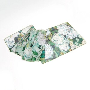 May include: A white silk scarf with a green floral print. The print features white roses and green leaves in a painterly style.