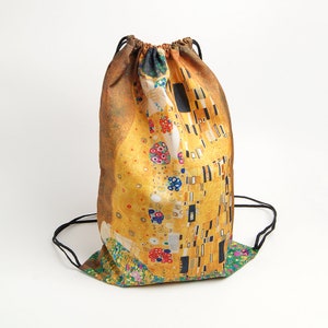 Könnte beinhalten: Eine Kordeltasche mit einem farbenfrohen Druck von Gustav Klimts Gemälde "Der Kuss". Die Tasche ist aus einem weichen, strapazierfähigen Stoff gefertigt und hat einen schwarzen Kordelzug.