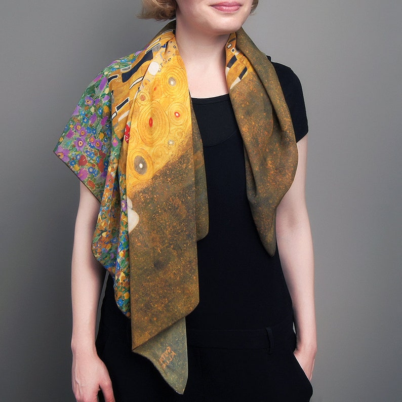May include: A silk scarf with a colorful floral pattern on one side and a painting of two figures embracing on the other side. The painting is in shades of gold, yellow, and brown. The scarf is folded and draped around a person's neck.