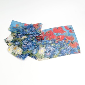 May include: A blue and white silk scarf with a floral print of red poppies and blue flowers. The scarf is folded and draped on a white surface.
