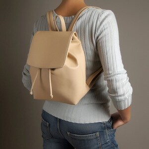 May include: A light beige leather backpack with a drawstring closure and adjustable straps.
