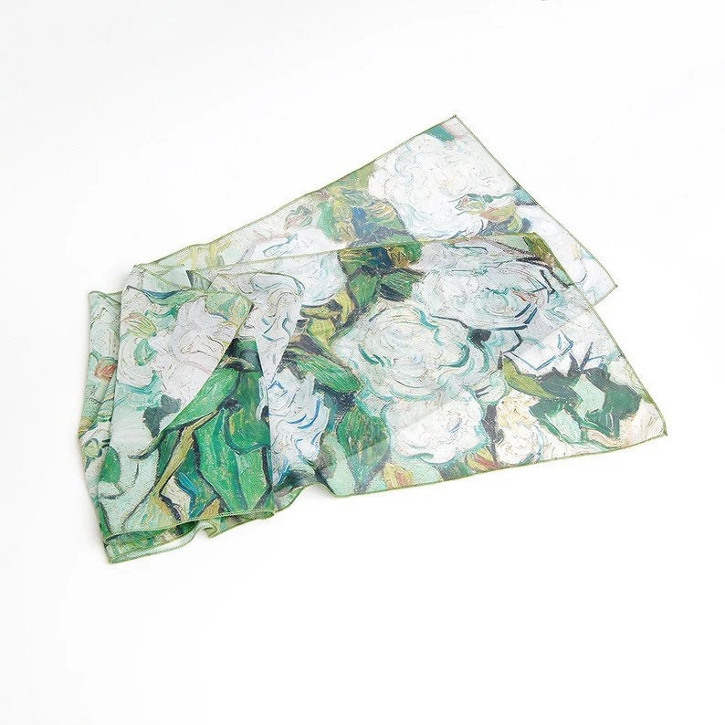 May include: A white silk scarf with a green and white floral print. The print is a reproduction of a famous painting of white roses.