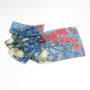 May include: A blue and white silk scarf with a floral print of red poppies, blue cornflowers, and white daisies. The scarf is folded and draped on a white surface.