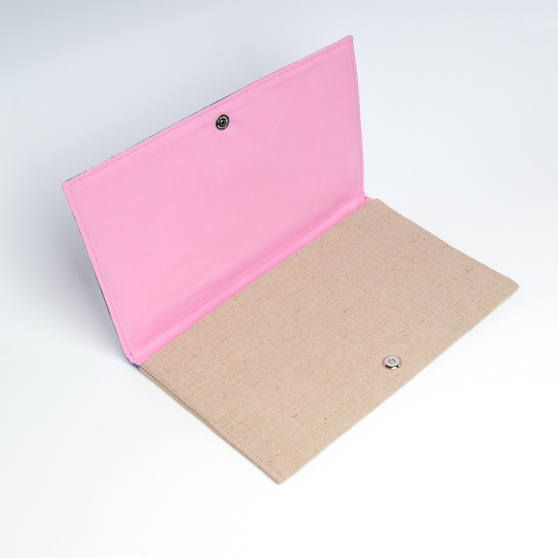 Puede incluir: Un embrague de tela rosa y beige con cierre a presi&oacute;n. El embrague est&aacute; abierto y el interior es visible. El interior est&aacute; forrado con una tela beige.