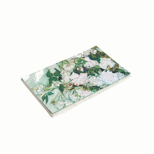 May include: A stack of white and green paper notepads with a painting of white flowers on a green background. The painting is a reproduction of a famous artwork.