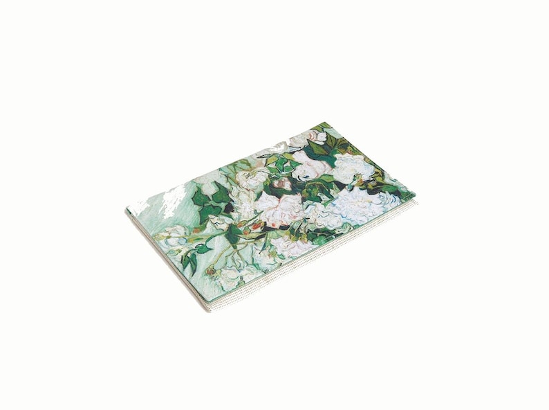 May include: A stack of white and green paper notepads with a painting of white flowers on a green background. The painting is a reproduction of a famous artwork.
