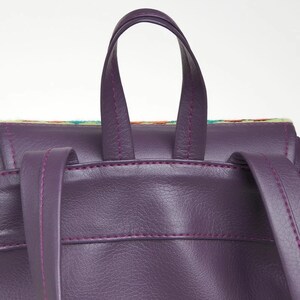 May include: Purple faux leather backpack with a top handle and adjustable straps. The backpack has a colorful patterned fabric lining the top edge.