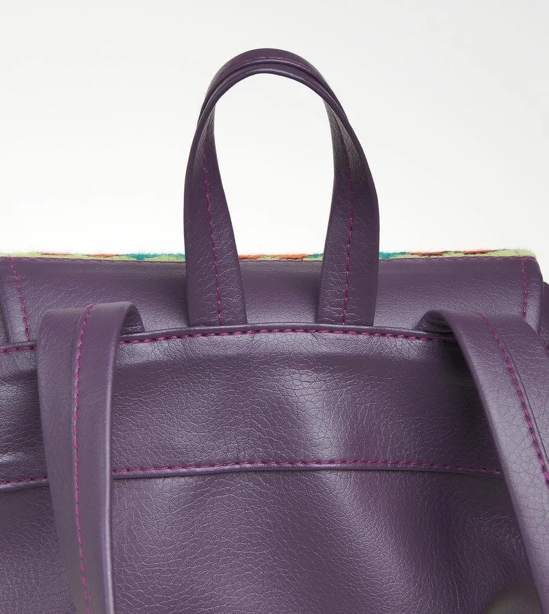 May include: Purple faux leather backpack with a top handle and adjustable straps. The backpack has a colorful patterned fabric lining the top edge.