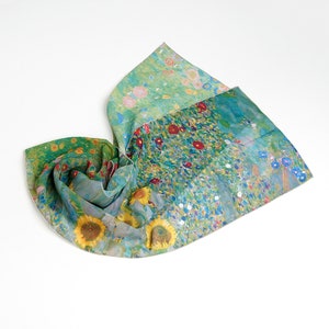 Könnte beinhalten: Ein Seidenschal mit farbenfrohem Blumenmuster, Sonnenblumen und roten Blüten auf grünem Grund. Der Schal ist gefaltet und zeigt das detailreiche Kunstwerk und die lebendigen Farben.