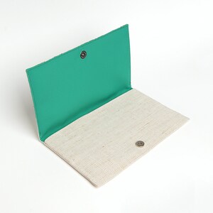May include: A white and green fabric clutch with a snap closure. The clutch is open and the inside is lined with a green fabric.