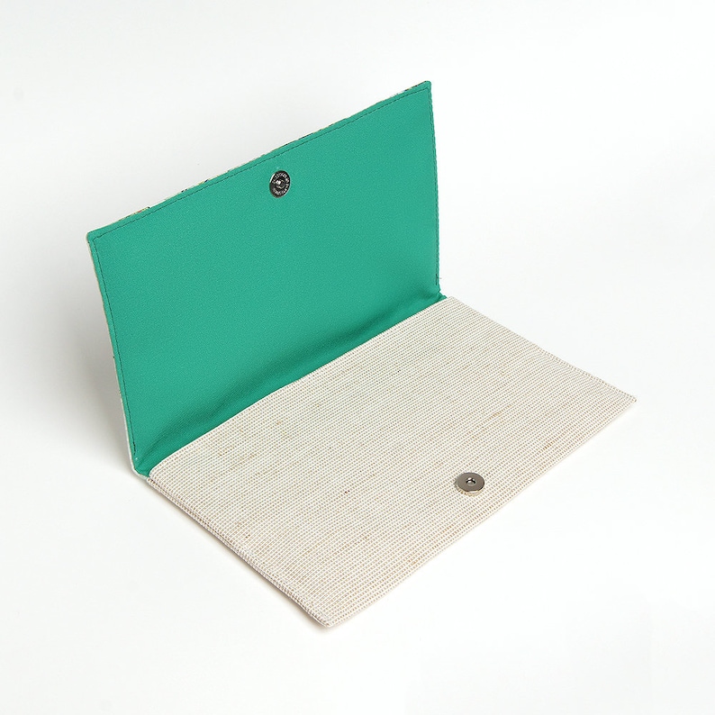 May include: A white and green fabric clutch with a snap closure. The clutch is open and the inside is lined with a green fabric.