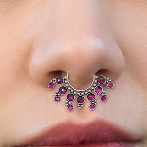Może przedstawiać: Srebrny kolczyk do nosa z okrągłym wzorem i różowymi kamieniami szlachetnymi. Kolczyk jest noszony w nosie osoby.