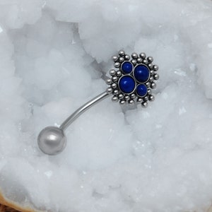 May include: Silver belly button ring with a cluster of blue gemstones in a flower shape.