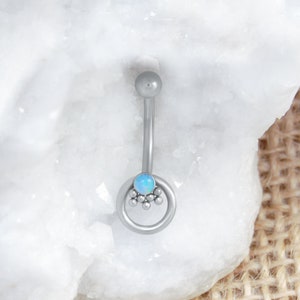 May include: Silver belly button ring with a small opal gemstone and a circle of small beads around it.
