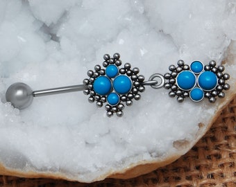 May include: A silver-toned belly button ring featuring a straight barbell with a smooth ball end and a decorative dangle charm. The charm consists of two ornate, textured silver-toned sections inlaid with small, round, bright turquoise blue stones.