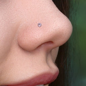 Op de afbeelding: Close-up van een gezicht met een kleine, heldere neusring. De persoon glimlacht en heeft zijn mond lichtjes open.