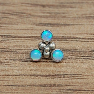 May include: A body jewelry piece featuring a triangular arrangement of three round, iridescent blue opal cabochons set in polished silver-toned metal, accented by a cluster of small, smooth, spherical metal beads at the center of the design.