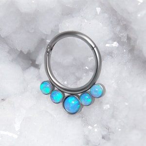 Pode incluir: Um brinco de argola de prata com cinco pedras de opala azul. A argola é sem costura e as pedras preciosas estão dispostas em uma fileira.