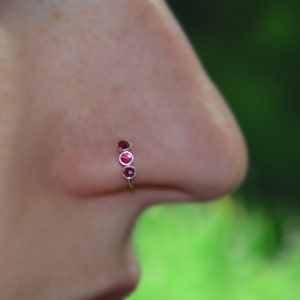 May include: A silver nose ring with three pink gemstones.
