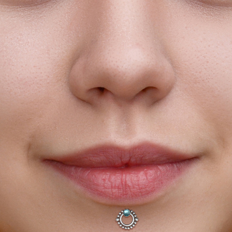 May include: Close-up of a person's lower face with a silver lip ring with a turquoise gemstone. The ring is in the center of the lower lip.