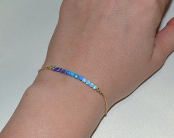 May include: A delicate gold chain bracelet with a row of small, iridescent opal beads in shades of purple, blue, and white.