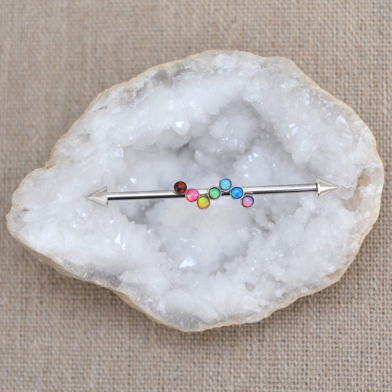 May include: A rainbow colored barbell with opal gems. The barbell is made of surgical steel and has a pointed end on each side.
