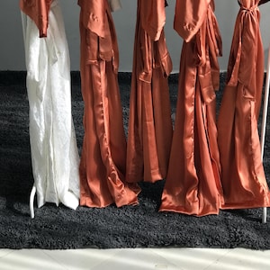 a row of orange satin robes hanging on a rack, with a black rug in the foreground.