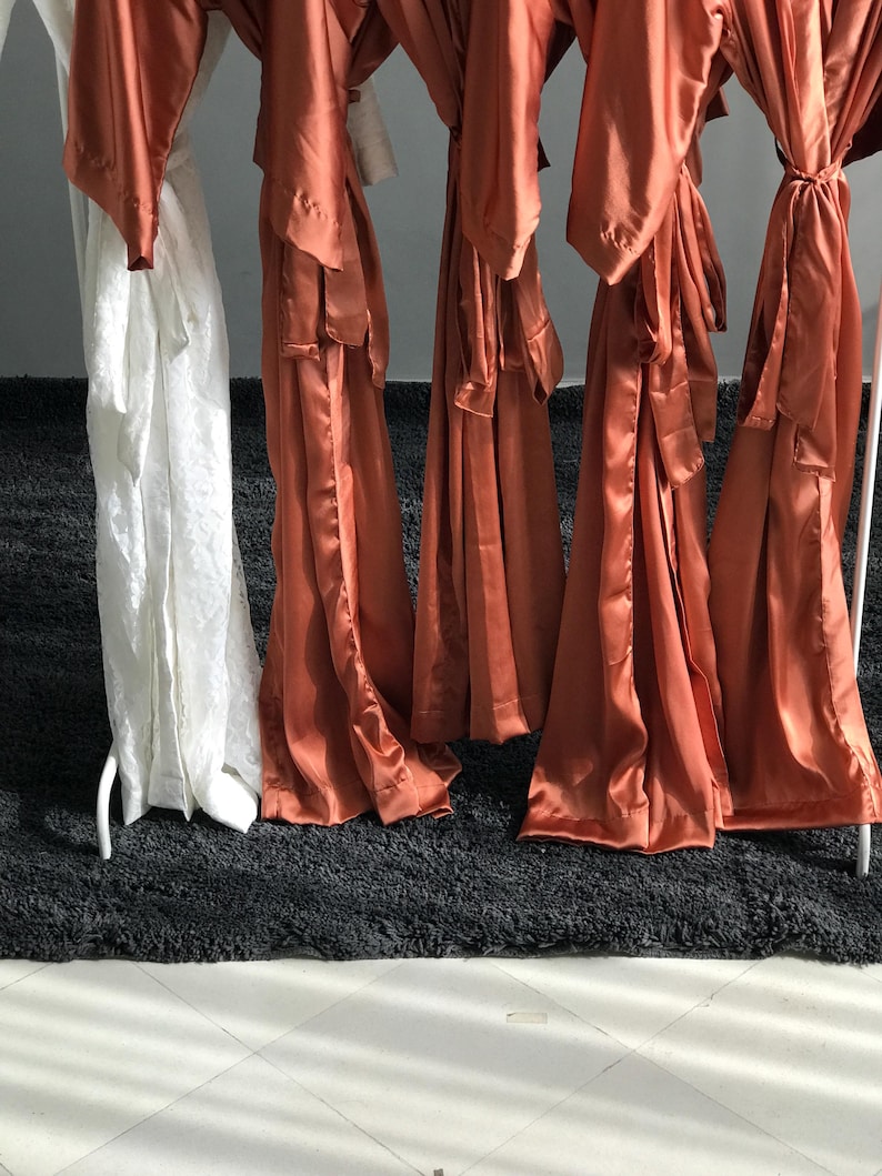 a row of orange satin robes hanging on a rack, with a black rug in the foreground.