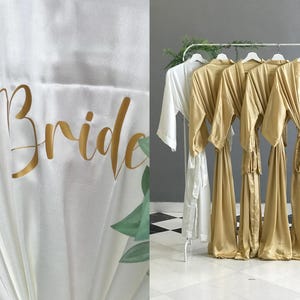 The image is a collage of two photos. The left photo shows a close-up of a white robe with the word "Bride" written on it in gold cursive text. The right photo depicts a row of gold satin robes hanging on a rack.