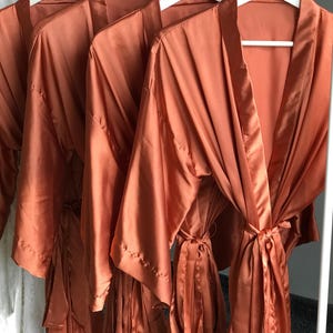 a collection of orange satin robes hanging on white hangers.