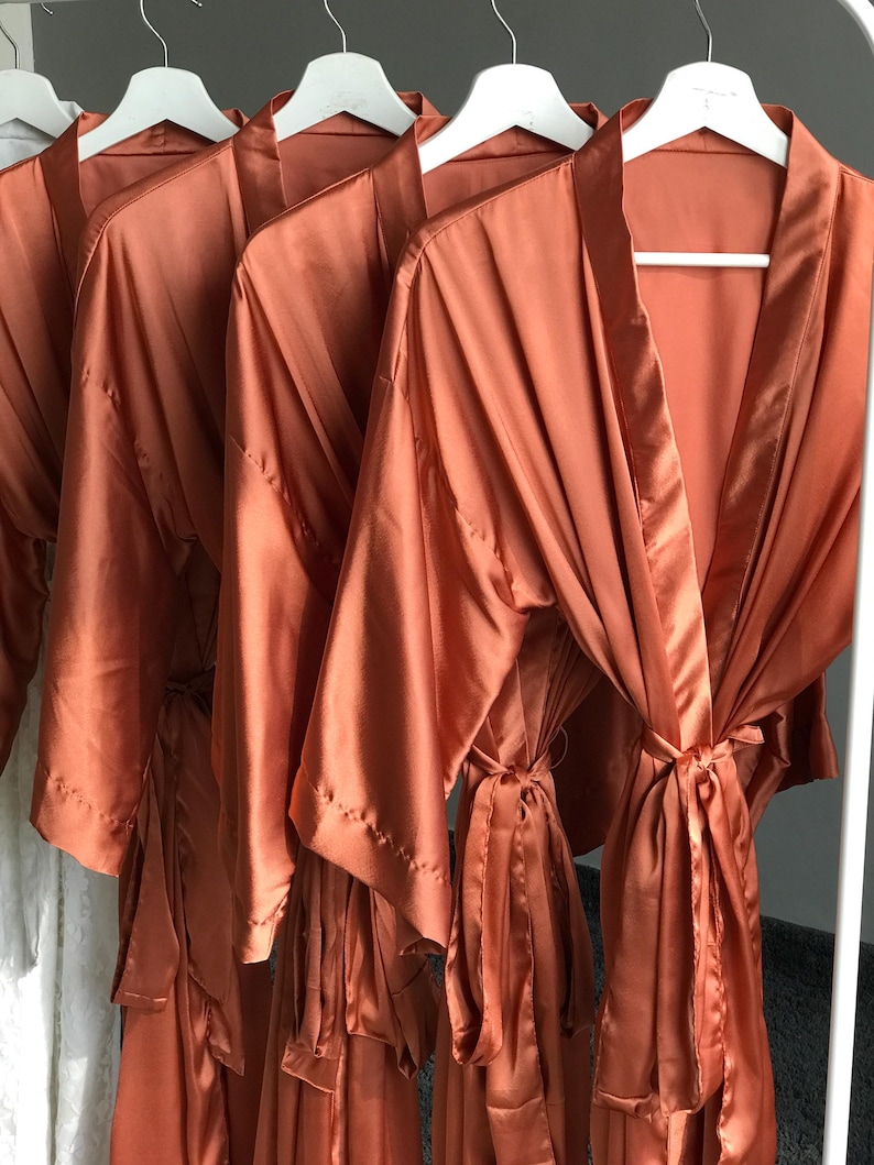 a collection of orange satin robes hanging on white hangers.