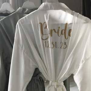 May include: White satin robe with the word "Bride" and the date "12.31.23" printed in gold on the back.