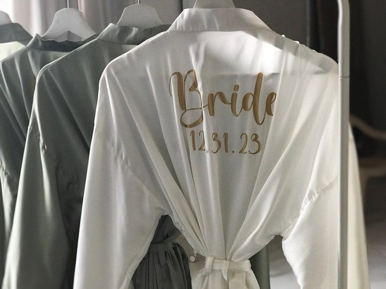May include: White satin robe with the word "Bride" and the date "12.31.23" printed in gold on the back.