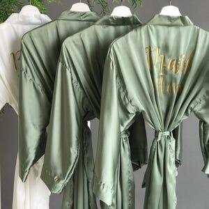 a row of three green satin robes with gold text on the back, hanging on a clothing rack.