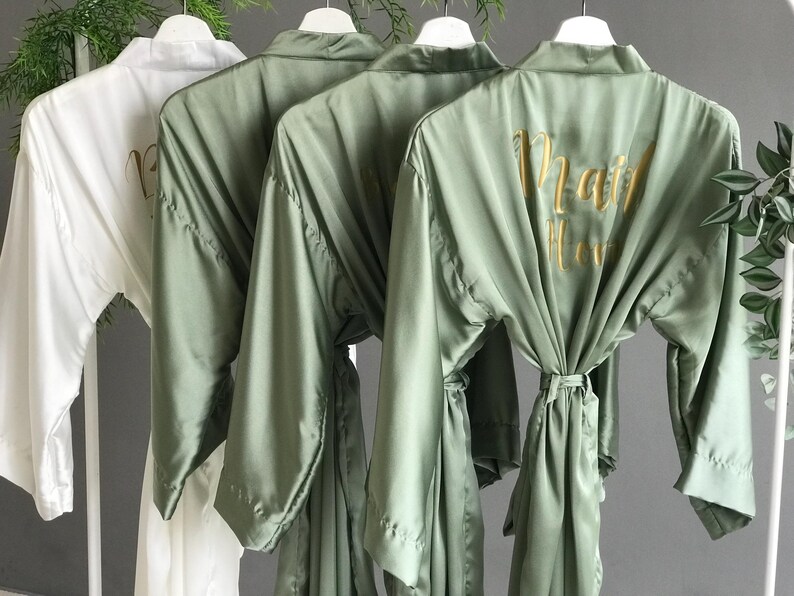 a row of three green satin robes with gold text on the back, hanging on a clothing rack.
