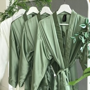 May include: Four satin robes hanging on white hangers. Three robes are sage green and one is white.