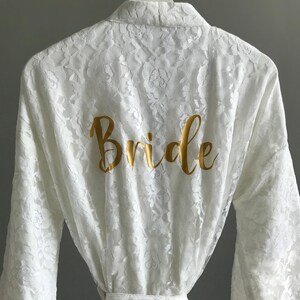 A white lace robe with the word "Bride" printed in gold on the back.