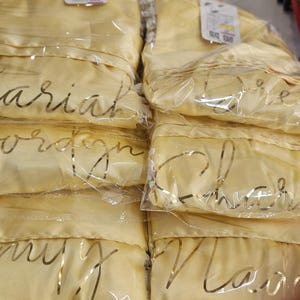 A close-up view of several yellow fabric items, possibly robes or pajamas, wrapped in clear plastic and labeled with the name "Carrie".